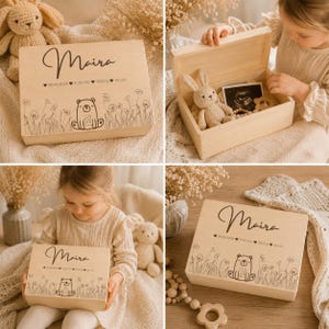 May include: A light-colored wooden keepsake box with the name "Maira" in cursive. The box is decorated with a bear illustration, flowers, and birth details. Inside, a stuffed bunny and baby items are visible.