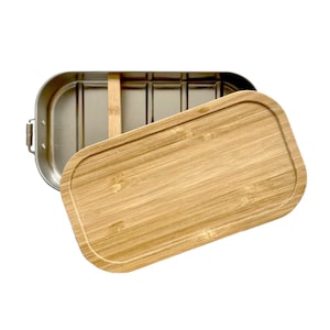Puede incluir: Una fiambrera rectangular de acero inoxidable con esquinas redondeadas y una tapa de bamb&uacute; extra&iacute;ble. El interior presenta un acabado met&aacute;lico con un divisor vertical de bamb&uacute; colocado en el centro del recipiente para separar.
