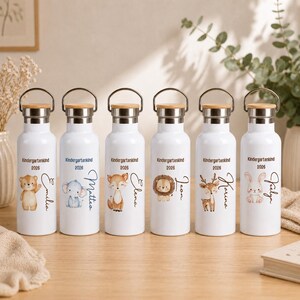 May include: Six white metal water bottles with silver rims and wooden lids. Each bottle features a unique watercolor animal illustration, the text "Kindergartenkind 2026," and a personalized name in cursive script: Emilia, Matteo, Elena, Leon, Karina, and Jeelyn.