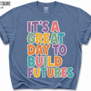 May include: Jeans blue t-shirt with the text "IT'S A GREAT DAY TO BUILD FUTURES" in colorful letters. The shirt is from Comfort Colors.