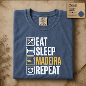 Puede incluir: Una camiseta azul vaquero con un gráfico de cuatro cuadrados apilados. El primero muestra un tenedor y una cuchara, el segundo una persona durmiendo, el tercero la isla de Madeira y el cuarto un icono de refrescar, con el texto EAT SLEEP MADEIRA REPEAT.