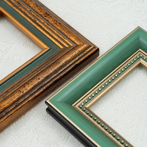 Puede incluir: Dos marcos de fotos rectangulares. Uno presenta un acabado en bronce envejecido y verde oscuro con molduras escalonadas. El segundo tiene una superficie lisa de color verde salvia, un borde interior dorado y un detalle de cuentas.