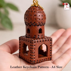 May include: A handcrafted brown leather keychain in the shape of a small building with a dome and arched windows. The keychain is held in a hand and has a gold-colored keyring. The text "Leather Keychain Pattern - A4 Size" is at the bottom.