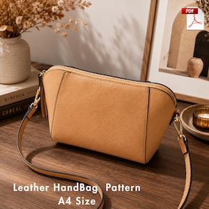 Puede incluir: Un bolso de mano de cuero color canela con superficie texturizada, cierre de cremallera superior curvado y una correa de hombro fina y ajustable sujeta con herrajes metálicos dorados. El texto "Leather HandBag Pattern A4 Size" es visible abajo.