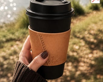 Puede incluir: Una taza de café negra con tapa negra se sostiene en una funda de cuero marrón. La funda tiene una costura cosida y un pequeño logotipo. El texto "Leather Cup Sleeve Pattern - A4 Size" está en la parte inferior de la imagen.