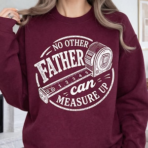 May include: Burgundy sweatshirt with a white graphic. The graphic reads "NO OTHER FATHER can MEASURE UP" with a measuring tape design. The sweatshirt is a solid burgundy colour.