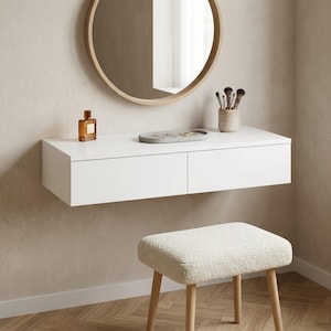 May include: A modern white floating vanity with two drawers, a round wooden-framed mirror, and a small stool with light wood legs and a cream-colored, textured seat. Accessories include a perfume bottle, makeup brushes, and a jewelry tray.