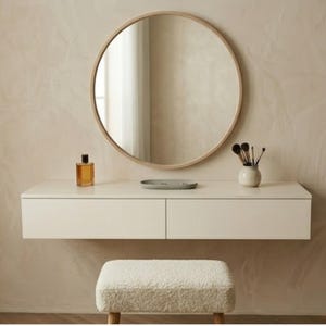 May include: A modern vanity set with a round wooden-framed mirror, a white floating drawer unit, and a fluffy white stool. Accessories include a perfume bottle, a small tray, and a vase with makeup brushes.