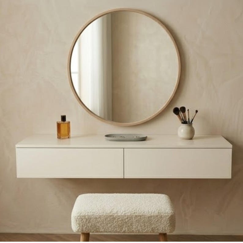 May include: A modern vanity set with a round wooden-framed mirror, a white floating drawer unit, and a fluffy white stool. Accessories include a perfume bottle, a small tray, and a vase with makeup brushes.