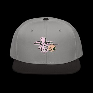 Puede incluir: Gorra de béisbol gris con visera negra. La gorra presenta el texto rosa "Durry Up" en cursiva, acompañado de un gráfico de calavera guiñando un ojo. La gorra tiene un botón negro en la parte superior.