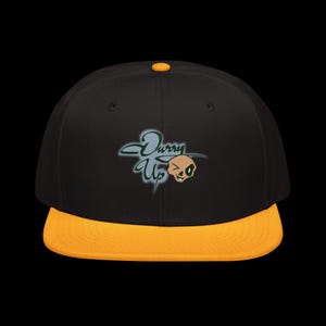 May include: Black and yellow flat-peak baseball cap. The cap has the text "Durry Up" in a stylized font with a winking skull graphic. The peak is yellow, and the crown of the cap is black.