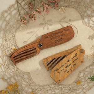 Peut inclure: Deux peignes pliants en bois avec des messages gravés. L'un dit "To my forever love always yours 2222" et l'autre dit "You mean the world to me, today and every day". Les peignes sont sur une nappe en dentelle avec des fleurs.