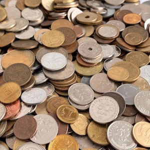 May include: A close-up shot of a pile of various coins. The coins are in different sizes, colors, and shapes. Some coins are gold, silver, and bronze. The coins are scattered and overlapping, creating a textured surface.