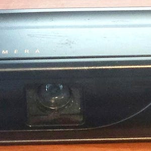 May include: A black Kodak Star 110 camera featuring a rectangular body, a built-in flash on the right side, a central lens, and a viewfinder. The top surface displays the text Kodak Star 110 Camera in gold and white lettering.