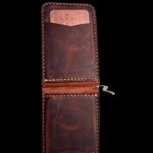 May include: Open, brown leather wallet with a silver money clip. The wallet has a card slot and visible stitching. A wooden card is visible inside the wallet.