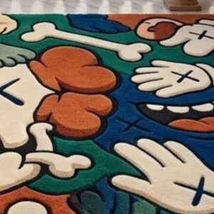 May include: A colorful rug featuring a cartoon-style design with a skull, bones, hands, and feet. The rug has a blue, green, orange, and off-white color scheme. The design includes cross-shaped eyes and hand details.