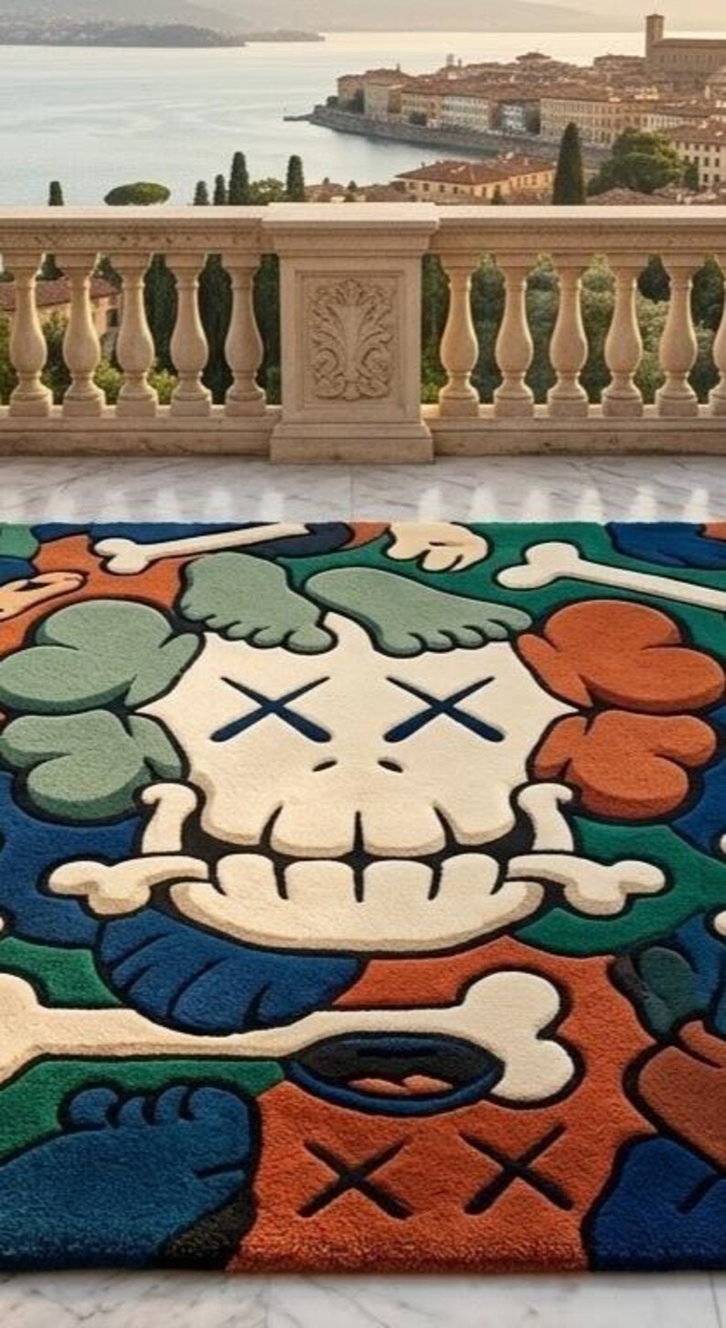 May include: A colorful rug featuring a cartoon skull design with crossed-out eyes and bone accents. The rug incorporates shades of blue, orange, green, and cream. The rug is placed on a marble surface with a scenic background.