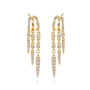 May include: A pair of gold-toned dangle earrings featuring three cascading chains of varying lengths. Each chain is adorned with small, clear, round-cut stones and terminates in a slender, pointed, stone-encrusted drop element.