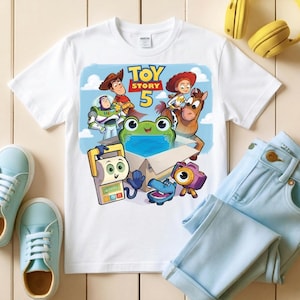 May include: White t-shirt featuring a colorful graphic from the movie Toy Story 5. The design includes characters like Woody, Buzz Lightyear, and Jessie. The shirt is paired with light blue jeans and sneakers.