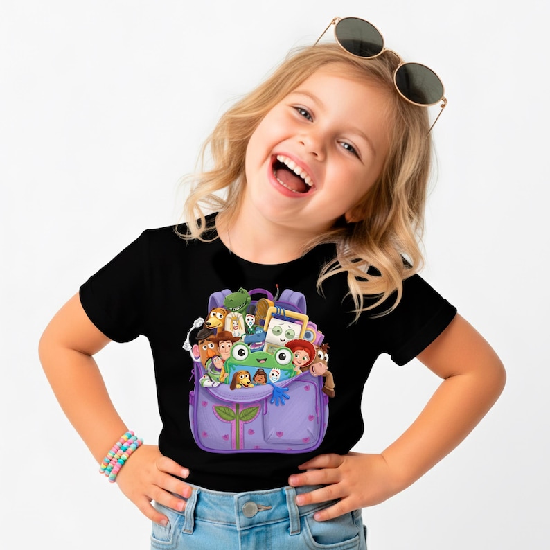 Pu&ograve; includere: T-shirt nero con grafica di zaino viola pieno di personaggi dei cartoni animati. Lo zaino ha due tasche e un motivo a foglie. La maglietta &egrave; girocollo ed &egrave; realizzata in materiale morbido.