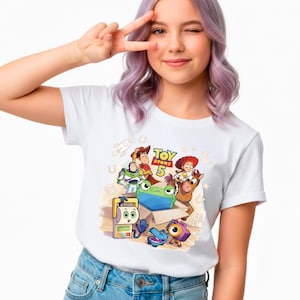 Pu&ograve; includere: T-shirt bianca con una grafica colorata dei personaggi del film "Toy Story 5". Il design include Woody, Buzz Lightyear, Jessie e altri personaggi. La maglietta &egrave; abbinata a jeans blu.