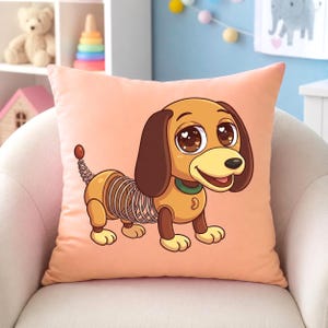 May include: A peach-colored square pillow featuring a cartoon dachshund with a spring-like body. The dog has brown ears, a green collar, and large, expressive eyes. The design is a playful, whimsical style, suitable for a child's room or nursery.