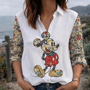 May include: A white button-down shirt featuring long sleeves with a multi-colored comic strip pattern. The center of the shirt displays a large graphic of Mickey Mouse, also filled with a colorful comic strip design, wearing red shorts and yellow shoes.