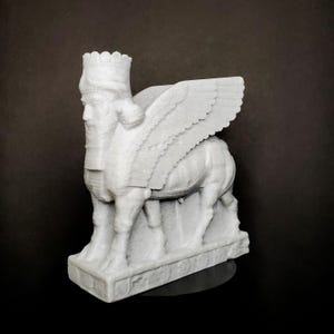 May include: A white, textured sculpture of a Lamassu, an ancient Mesopotamian protective deity. The figure features a human head with a crown and beard, combined with the body of a bull and large, detailed wings, all standing on a rectangular base.
