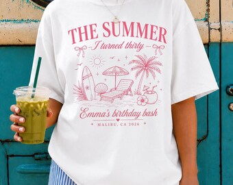 May include: A white short-sleeve t-shirt featuring a pink graphic print with the text THE SUMMER I turned thirty, Emma's birthday bash, and MALIBU, CA 2026. The design includes a surfboard, beach chair, palm tree, and tropical drink.