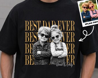 May include: A black t-shirt featuring a repeating gold text graphic that reads BEST DAD EVER. Centered is a black and white photograph of two children wearing sunglasses with their arms crossed. The name David & Emily is written below.