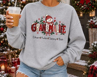 May include: A light gray crewneck sweatshirt featuring a graphic of a snowman wearing a red plaid hat and scarf. The text reads "GRANDMALIFE" in red plaid lettering, with the names "Ethan", "Katie", "Sammy", and "Bob" printed below.