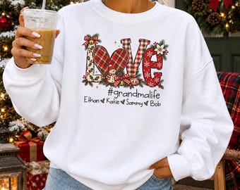 May include: A white long-sleeve sweatshirt featuring the word LOVE in a festive holiday pattern with a plaid heart, a snowman, and greenery. Below the text, it reads #grandmalife followed by the names Ethan, Katie, Sammy, and Bob.