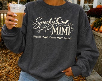 May include: A dark charcoal gray crewneck sweatshirt featuring a cream-colored graphic with the text Spooky MIMI, a crescent moon, stars, and bat silhouettes. Below the main text, the names Sophia, James, and Daniel are printed with small bats.