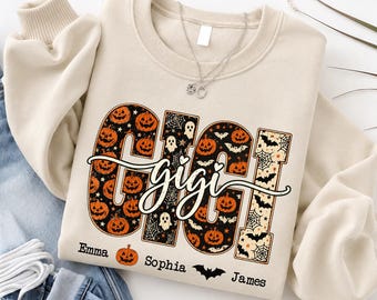 May include: A cream-colored crewneck sweatshirt featuring a large graphic with the text "GIGI" in block letters filled with orange pumpkins, white ghosts, and black bats on a spiderweb background. Below, the names "Emma", "Sophia", and "James" are printed.
