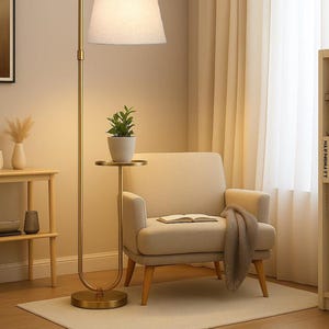 May include: A gold-toned floor lamp with a white lampshade illuminates a cozy living space. A small side table holds a potted plant. An armchair with a blanket and an open book sits on a neutral rug.