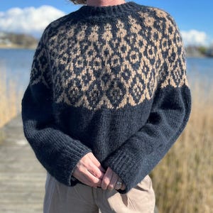 May include: A dark blue and tan patterned sweater. The upper portion features a geometric design in tan, while the lower section and sleeves are solid dark blue. The sweater has a crew neck and a relaxed fit, suitable for cooler weather.