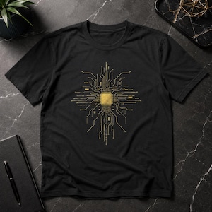 May include: A black short-sleeve t-shirt featuring a gold-colored graphic print of a central computer processor chip with intricate circuit board lines radiating outward in a symmetrical pattern across the chest area of the garment.