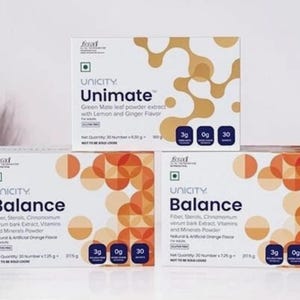 May include: Three white boxes of Unicity supplements are stacked on a white surface. The top box is labeled "Unimate" with lemon and ginger flavor. The bottom two boxes are labeled "Balance" with orange flavor. Each box has a nutritional information section.