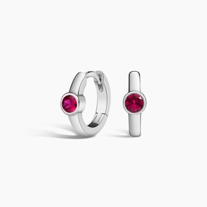 Peut inclure: Une paire de créoles en argent avec une pierre précieuse rose vif de taille ronde sertie au centre de chaque anneau. Les boucles d'oreilles présentent une finition métallique polie et un mécanisme de fermeture à charnière, au design épuré.