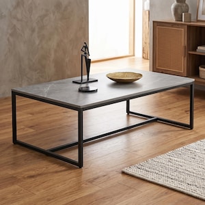 Peut inclure: Une table basse rectangulaire dotée d'un plateau à motif marbre gris et d'un cadre en métal noir. La surface de la table supporte une sculpture abstraite noire, un petit dessous de verre rond en marbre noir et un bol décoratif doré texturé.