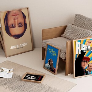 May include: A collection of framed movie posters, including "Jim & Andy," "Call Me by Your Name," and "Rushmore," displayed near a modern armchair and a small wooden side table. A rug and open magazine complete the interior design.