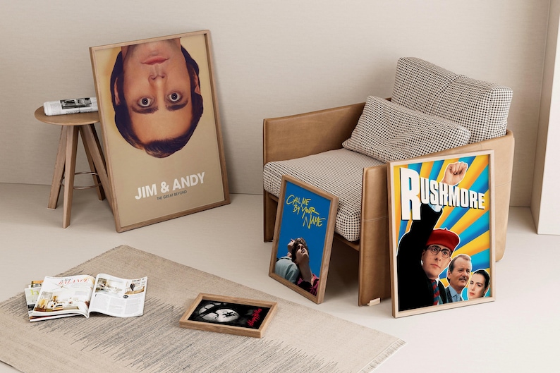 May include: A collection of framed movie posters, including "Jim & Andy," "Call Me by Your Name," and "Rushmore," displayed near a modern armchair and a small wooden side table. A rug and open magazine complete the interior design.