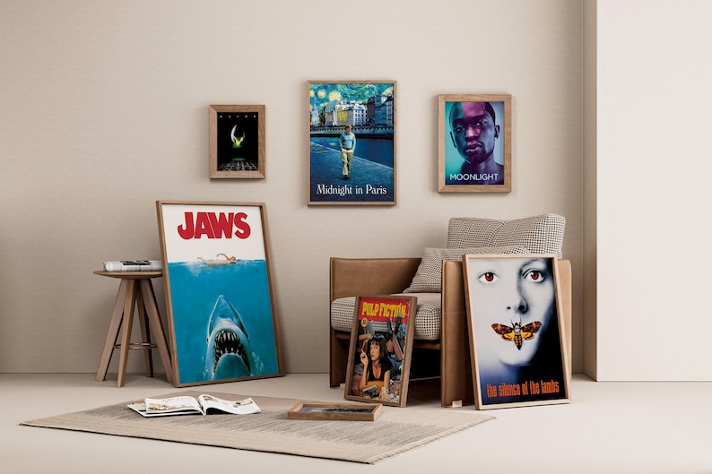 May include: A collection of framed movie posters, including "Jaws," "Midnight in Paris," "Moonlight," "Pulp Fiction," and "The Silence of the Lambs." The posters are displayed on a neutral-toned wall, with a rug and small wooden table.