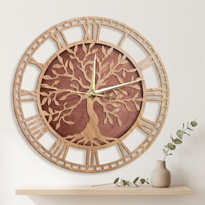 May include: A wooden wall clock with a tree of life design. The clock features Roman numerals and gold-colored hands. The tree design is in the center, with a dark brown background. The clock is made of light brown wood.
