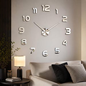Peut inclure: Une grande horloge murale composée de chiffres réfléchissants argentés disposés en cercle. L'horloge possède un mécanisme central circulaire avec deux longues aiguilles argentées fines et pointues indiquant l'heure sur le mur.