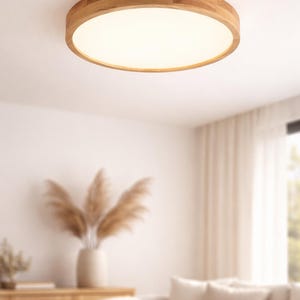 May include: A circular flush-mount ceiling light with a wooden trim. The light panel is bright white. The fixture is mounted on a white ceiling. The background shows a blurred living room with a sofa and cabinet.