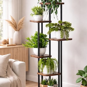Puede incluir: Un estante para plantas de varios niveles con soportes de metal negro y estantes de madera oscura. El estante contiene varias plantas en macetas con follaje verde, incluyendo helechos y plantas frondosas. La habitación está bien iluminada.