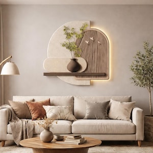 Può includere: Un soggiorno dai toni neutri con un divano beige e vari cuscini marroni e grigi. Un tavolino in legno espone un vaso con fiori secchi e libri. Arte murale con un vaso di verde e un pannello decorativo in legno.