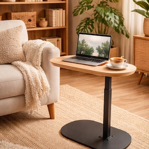 May include: A light wood laptop table with a black base and adjustable height. A laptop and a cup of coffee sit on the table. The table is next to a beige sofa and a woven rug.