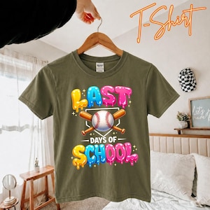Peut inclure: T-shirt vert olive avec un graphisme coloré. Le graphisme présente les mots "LAST DAYS OF SCHOOL" avec une balle de baseball et des battes croisées. Le texte est en jaune, bleu, rose et violet avec un effet dégoulinant.